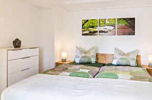 Une chambre à coucher avec un lit, deux tables de chevet, un tableau accroché au mur et une petite statue posée sur une commode.