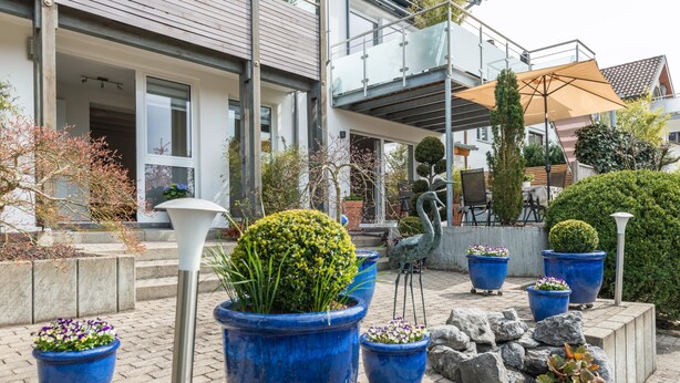 Ein modernes Gebäude mit Balkon, Sitzgelegenheit im Freien und Topfpflanzen.
