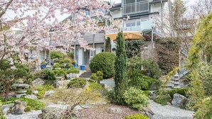 Ein traditioneller japanischer Garten mit Steinputzen, verschiedenen Sträuchern und einem Gebäude mit Balkon im Hintergrund.