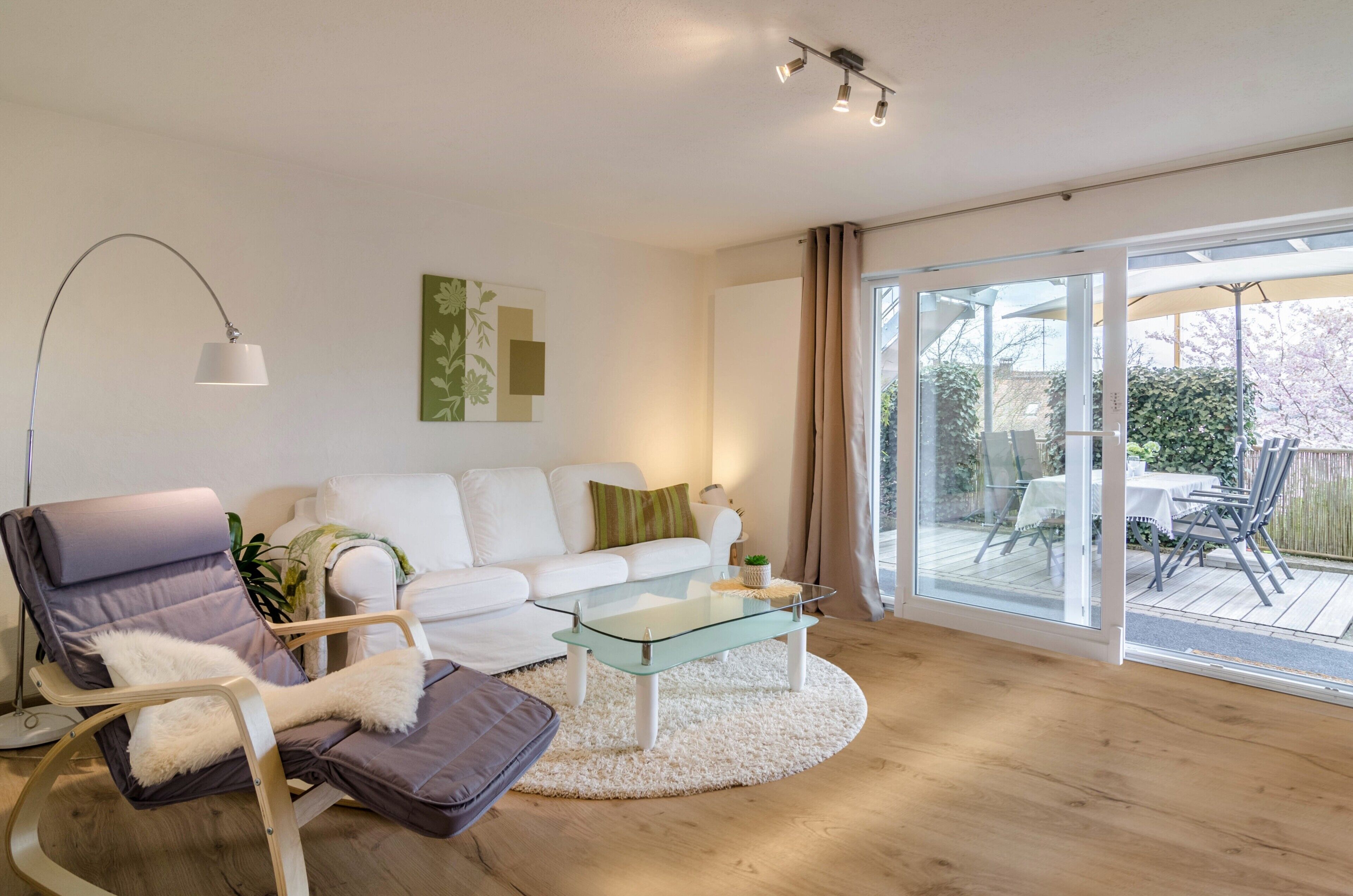 Un salon moderne avec un canapé blanc, une table basse en verre, un fauteuil inclinable et une lampe sur pied.