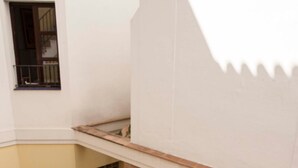A corner of a room with a tiled floor, a wooden bench, and a small window with a metal grille. - Center, luminous apt - 2 bathrooms (Sevilla)