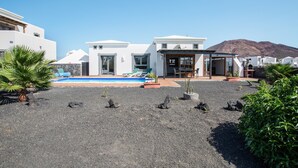 A modern villa with a pool, surrounded by volcanic rock and greenery. - Beautiful Holiday Home “Casa Violeta” with Terraces and Pool (Playa Blanca)