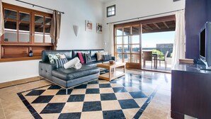 A living room with a checkered floor, a sofa, a coffee table, and a TV. - Beautiful Holiday Home “Casa Violeta” with Terraces and Pool (Playa Blanca)