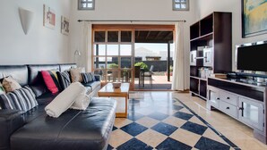 A living room with a black leather sofa, a coffee table, a TV, and a checkered floor. - Beautiful Holiday Home “Casa Violeta” with Terraces and Pool (Playa Blanca)
