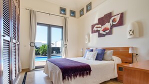 A bedroom with a bed, a nightstand, a lamp, a window with curtains, and a view of the outside. - Beautiful Holiday Home “Casa Violeta” with Terraces and Pool (Playa Blanca)