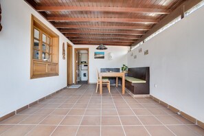 A hallway with a wooden ceiling, tiled floor, a table with chairs, a bench, and a door leading to another room. - Beautiful Holiday Home “Casa Violeta” with Terraces and Pool (Playa Blanca)