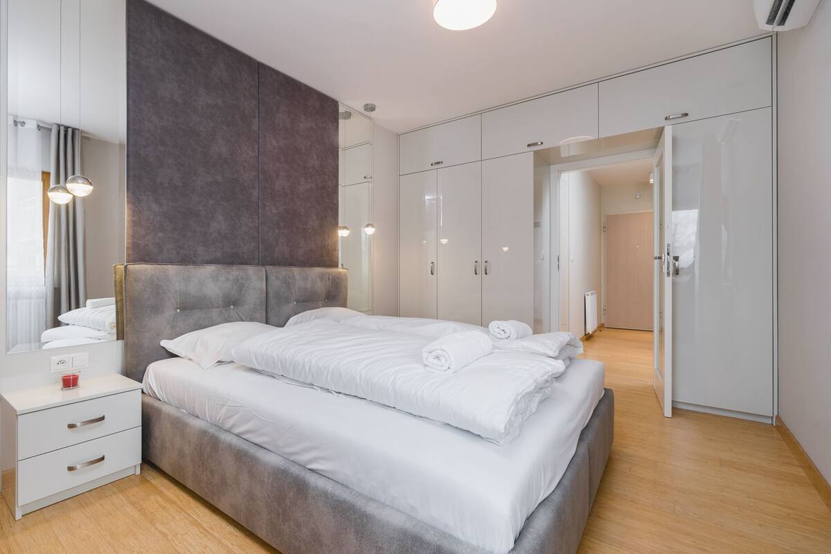 Une chambre à coucher moderne avec un grand lit, une table de chevet, un miroir et une armoire.