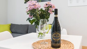 Amaro della Verretta -pullo on asetettu valkoiselle pöydälle, jonka päällä on kudottu alusta. Taustalla on vaasi, jossa on vaaleanpunaisia kukkia, ja lasi vettä.