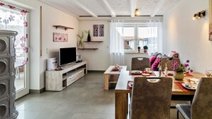 Een moderne woonkamer met een flatscreen televisie, houten meubels en een eethoek met een tafel gedekt voor twee personen.