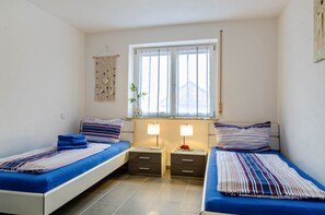 A twin room with two beds, bedside tables, a window with curtains, and a macrame wall hanging.
