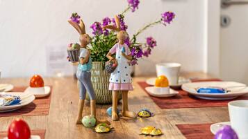 Una mesa de comedor con figuritas de conejo de cerámica, un florero con flores moradas y varios alimentos.