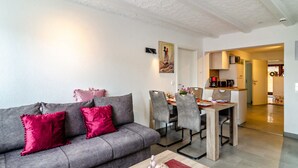 Een moderne woonkamer met een grijze bank, rode kussens, een salontafel en een eethoek met stoelen en een tafel.