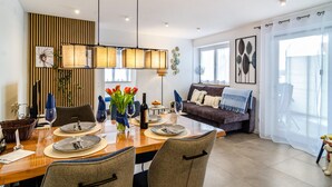 A dining area with a wooden table set for four, a sofa, and a large window with sheer curtains.