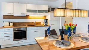 A modern kitchen with white cabinets, a wooden countertop, and a dining area set with plates, glasses, and a bottle.