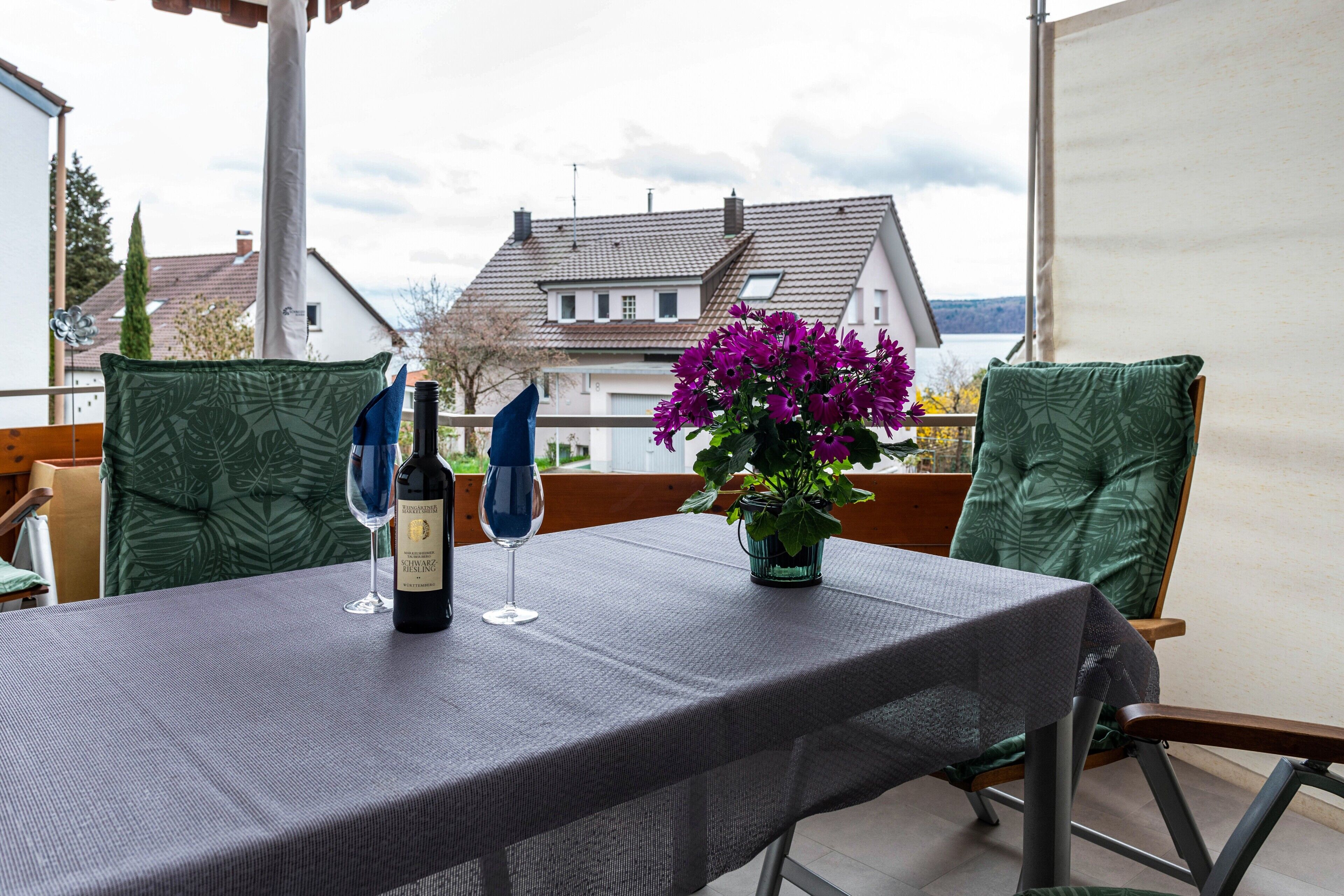 A table set outdoors with a tablecloth, two wine glasses, and a bottle of wine.