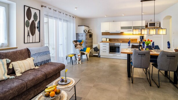 A modern living room with a brown sofa, a dining table with chairs, and a kitchen in the background.