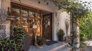 A building entrance with a wooden door, a stone bench, and various potted plants.