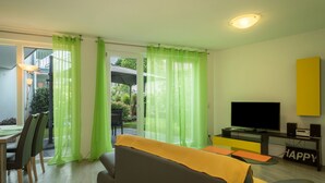 A living room with a sofa, TV, and a glass coffee table. - Apartment 'Jasmin' with Large Terrace and View of the Beautiful Flower Garden (Sipplingen am Bodensee)