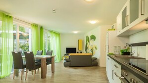 A modern kitchen with a dining area, a sofa, and a TV. - Apartment 'Jasmin' with Large Terrace and View of the Beautiful Flower Garden (Sipplingen am Bodensee)