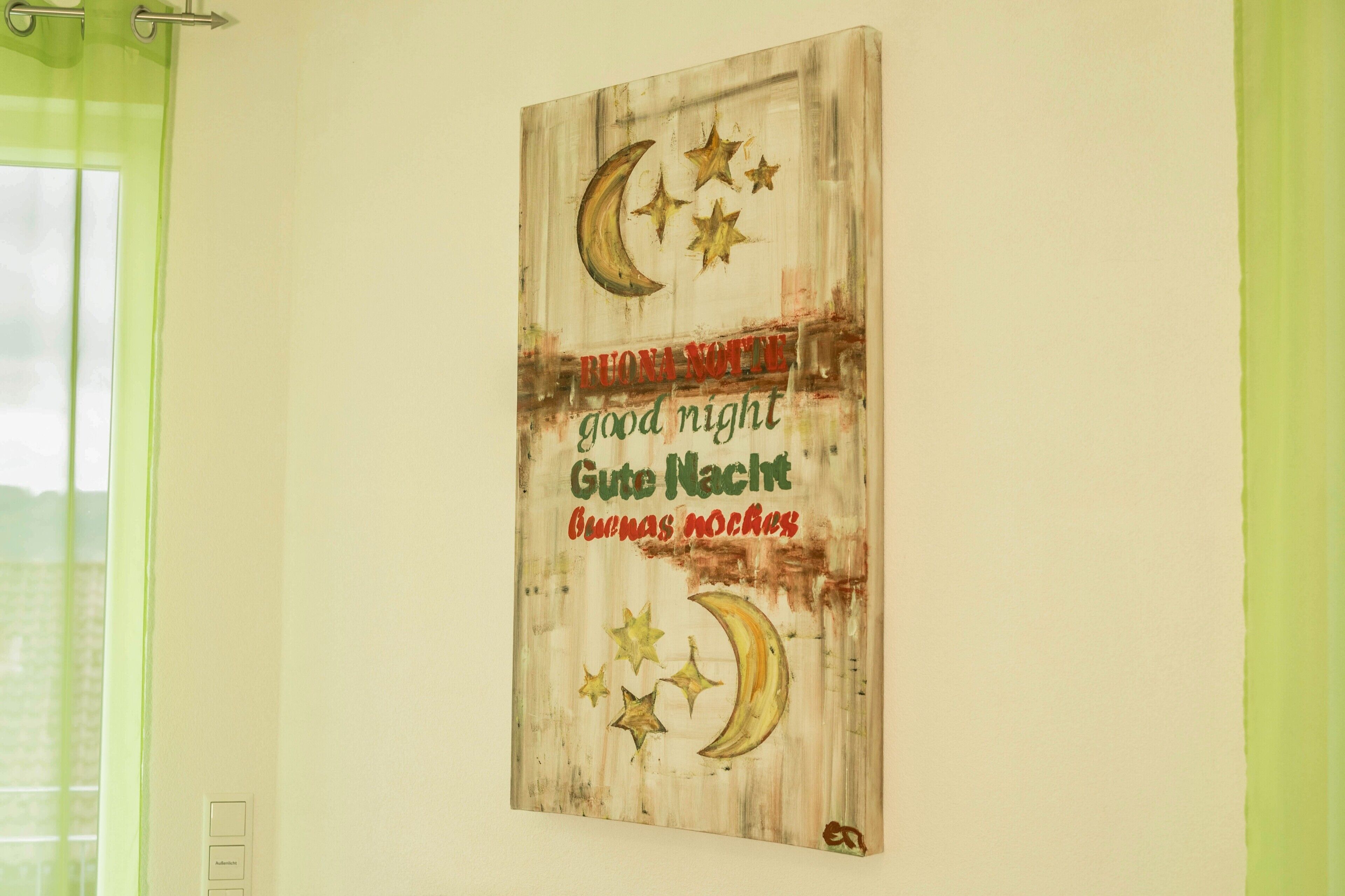 A wall with a rustic artwork featuring a crescent moon, stars, and multilingual 'good night' text.