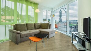 Una sala de estar moderna con un sofá seccional, una mesita, un televisor y ventanas amplias con vistas.