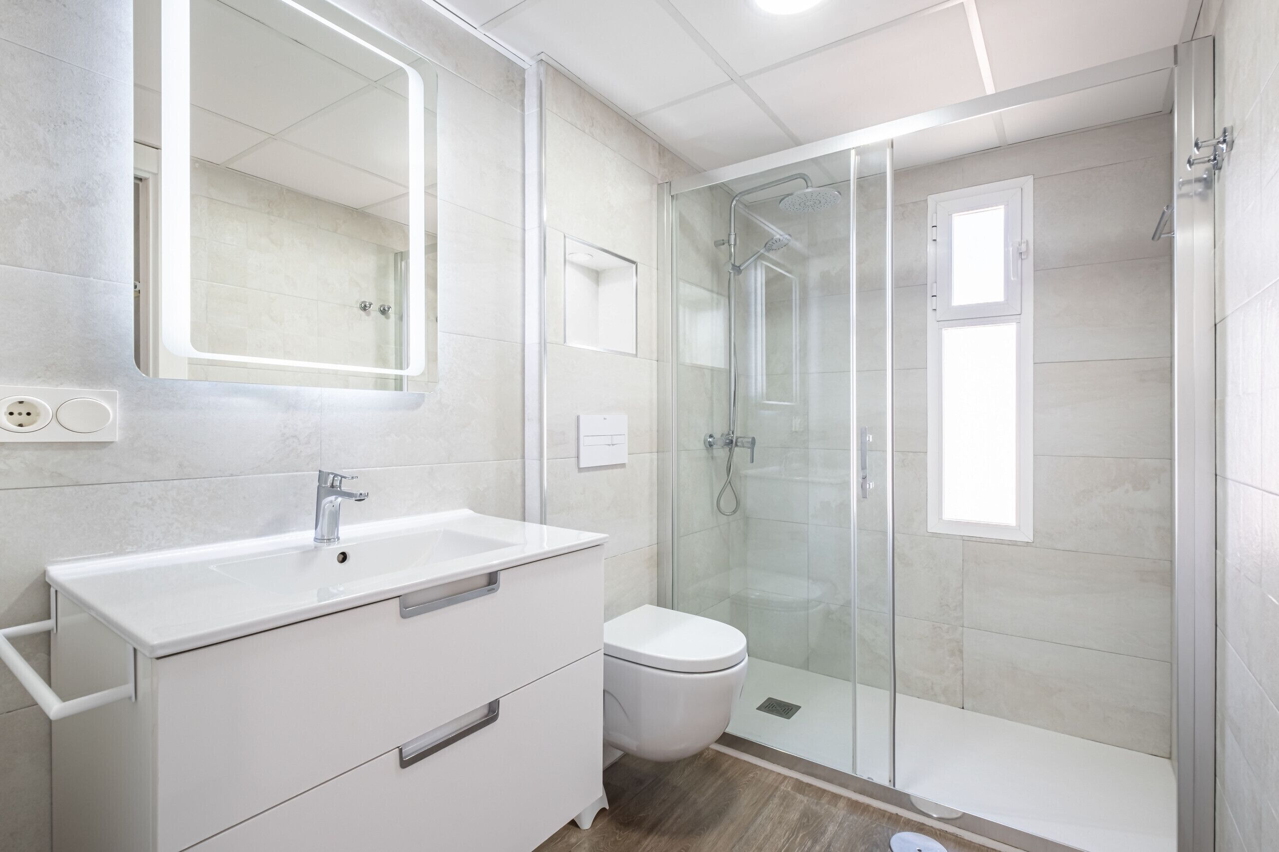 Un baño moderno con ducha de vidrio, lavamanos blanco y retrete.