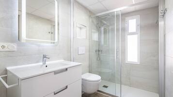 Un baño moderno con ducha de vidrio, lavamanos blanco y retrete.