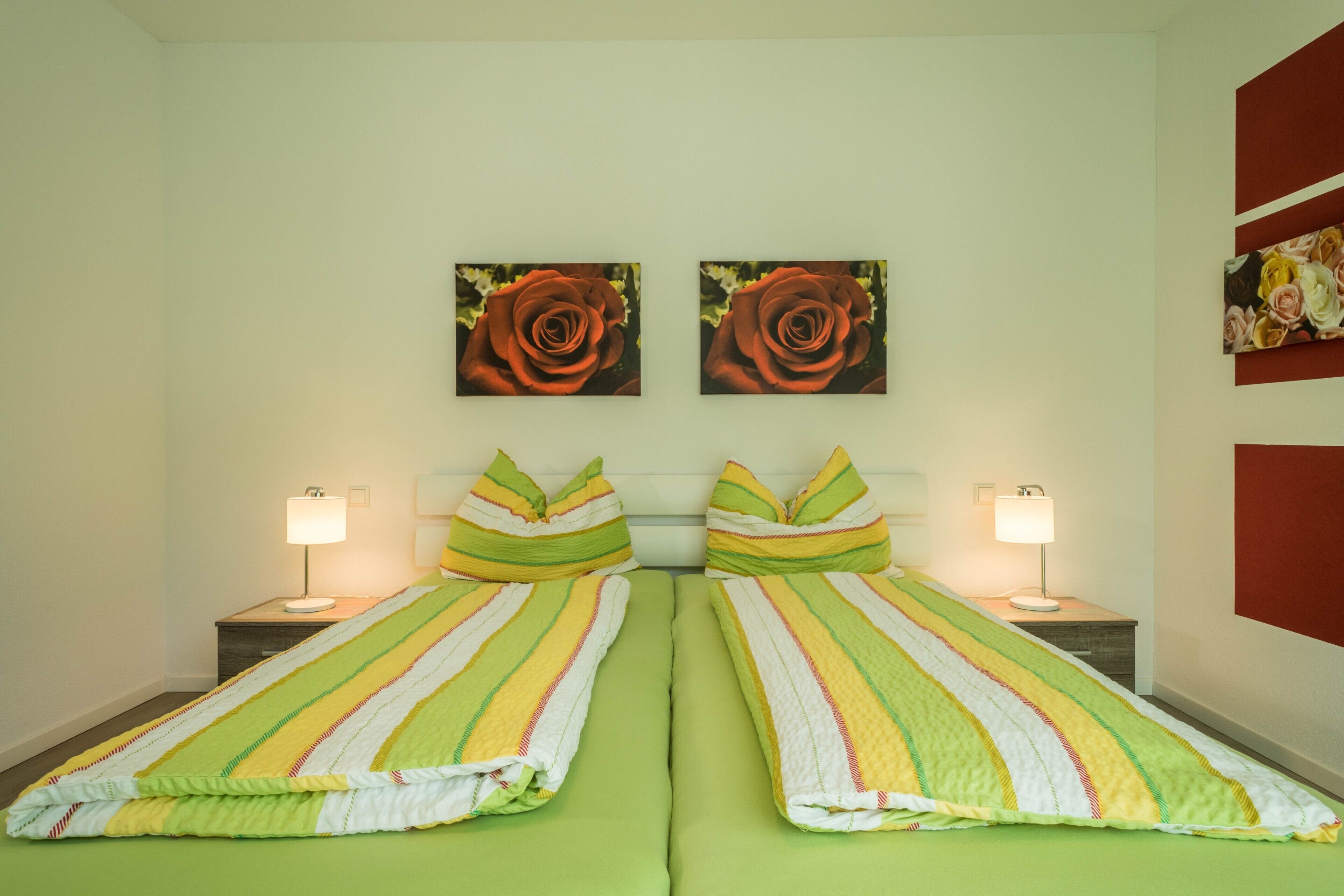 A twin room with two beds, green bedding, matching pillows, bedside lamps, and two rose paintings on the wall.