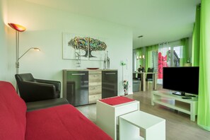 Una sala de estar moderna con un sofá, una mesa de centro, un televisor, un comedor con mesa y sillas, y una cocina con armarios y un refrigerador.