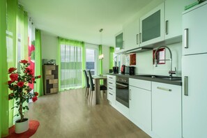 Una cocina moderna con armarios blancos, horno empotrado y comedor con mesa y sillas.