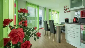 A modern kitchen with a dining area, green curtains, and a large window. - Apartment "Rose" with Large Balcony and Stunning Lake, Forest, and Mountain Views (Sipplingen am Bodensee)