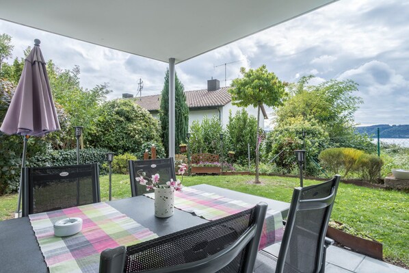 An outdoor patio with a table set for dining, surrounded by greenery and a view of a lake.
