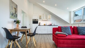 A modern kitchen with white cabinets, a red sofa, and a dining area with a wooden table and black chairs.