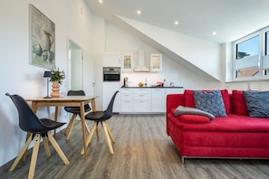 A modern kitchen with white cabinets, a red sofa, and a dining area with a wooden table and black chairs.