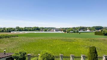 A large green field with a white building in the distance, surrounded by trees and a clear sky.
