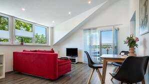 A modern living room with a red sofa, a TV, and a dining area with chairs and a table.