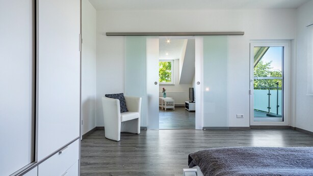 A modern bedroom with a bed, a chair, a small table, and a view of the outdoors.