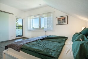 A bedroom with a bed, a window with curtains, a radiator, and a door leading to an outdoor balcony.