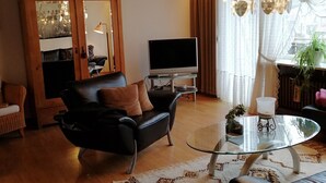 En moderne stue med en sort lædersofa, et glasbord, et træskab og et fjernsyn.