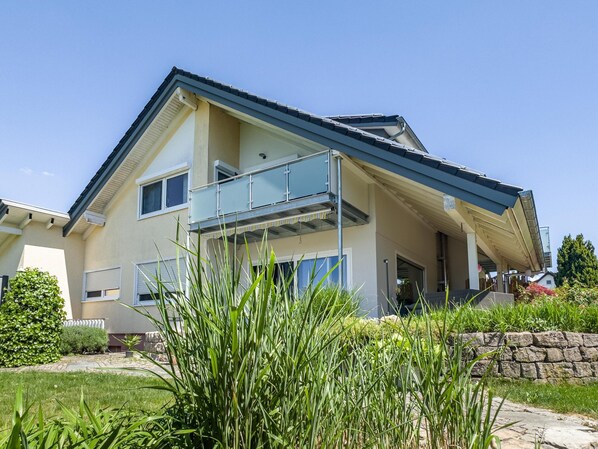 A two-story house with a balcony, a stone wall, and a grassy yard.