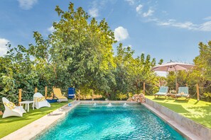 Piscina con sillones de descanso, una mesa y un área cubierta con sombrilla.