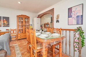 Un coin repas avec une table ronde dressée pour six personnes, des chaises en bois, un buffet avec des portes en verre et un miroir au-dessus de la cheminée.
