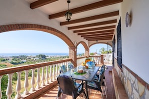 A terrace with a table set for dining, a view of the sea, and a balcony railing.