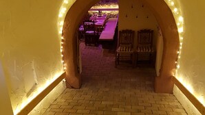 An arched hallway with brick flooring and illuminated walls, leading to a dining area with tables and chairs. - Beim Schloß Michel (Lauda)