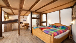 A wooden-framed bedroom with a bed, a wooden floor, and a kitchen area visible through an open doorway. - Beim Schloß Michel (Lauda)