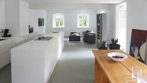 A modern kitchen with a central island, a dining area with a wooden table, and a bookshelf. - Ferienwohnungen Mittermurnthal (Neunburg vorm Wald)