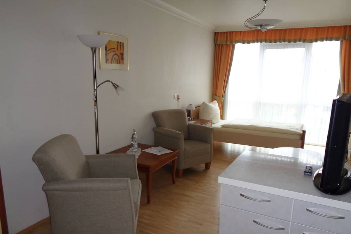 Quarto de hotel com sofá, poltrona, mesa pequena com uma garrafa, televisão e cama com cortinas.