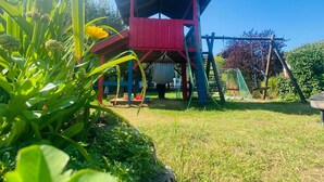A red playhouse with a slide and climbing net, surrounded by greenery and a clear blue sky. - Ferienhof Neukirchinger (Tiefenbach)