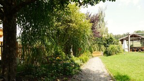 A paved pathway in a garden with trees and a wooden structure in the background. - Ferienhof Neukirchinger (Tiefenbach)