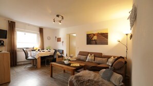 A cozy living room with a sofa, coffee table, and a dining area with a table and chairs. - Ferienhof Neukirchinger (Tiefenbach)